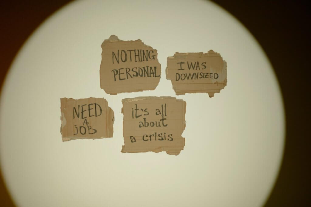 Photo de bouts de papier déchirés accrochés sur le mur sur lesquels sont écrits à la main "need a job" "nothing personnal" "it's all about crisis"