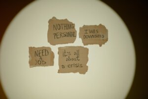 Photo de bouts de papier déchirés accrochés sur le mur sur lesquels sont écrits à la main "need a job" "nothing personnal" "it's all about crisis"